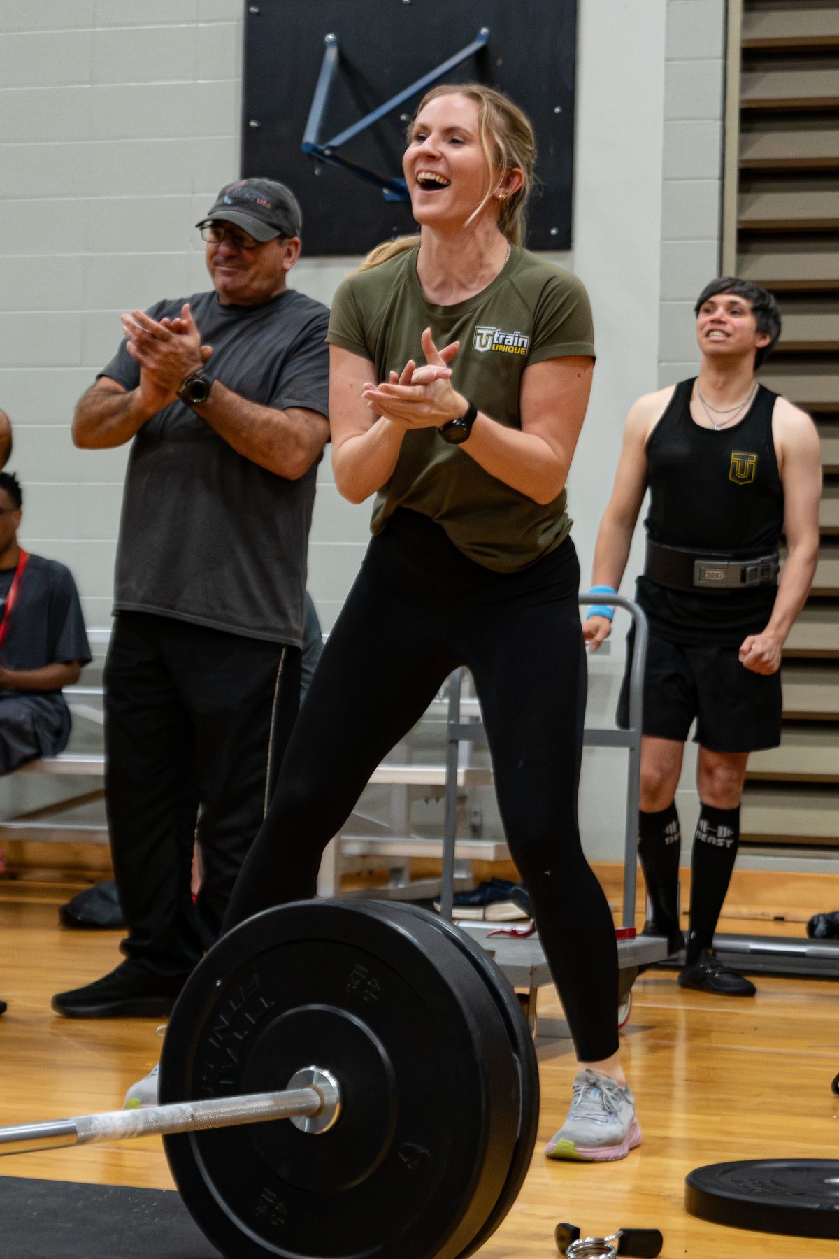 Two people clap and cheer beside a loaded barbell at Ulympics
