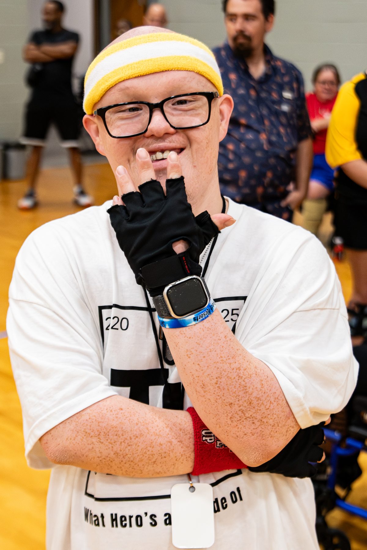 An athlete in a yellow headband and Train Unique shirt grins and strikes a thinking pose