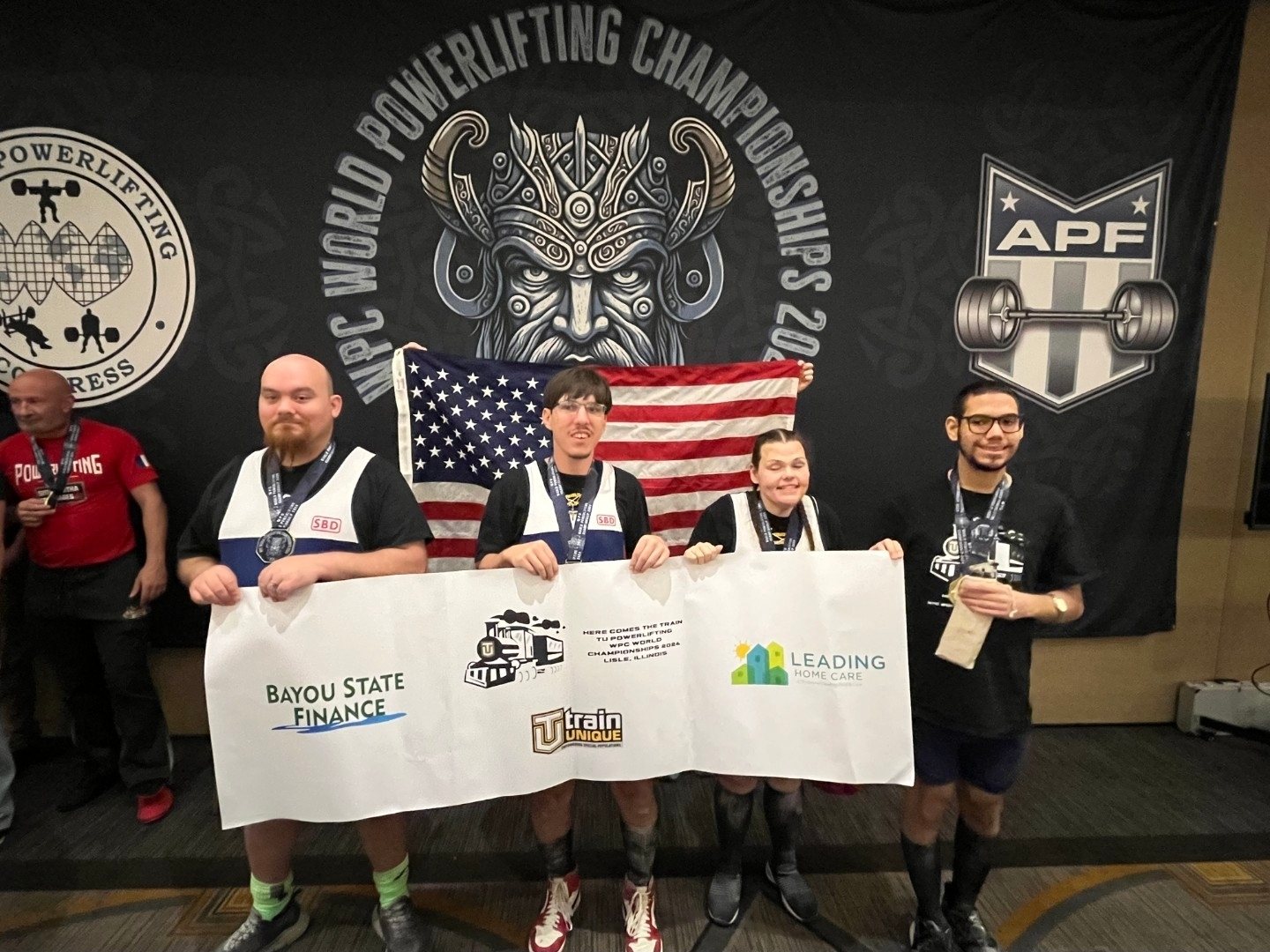 Four Train Unique lifters with the American flag and team banner at the WPC World Championships