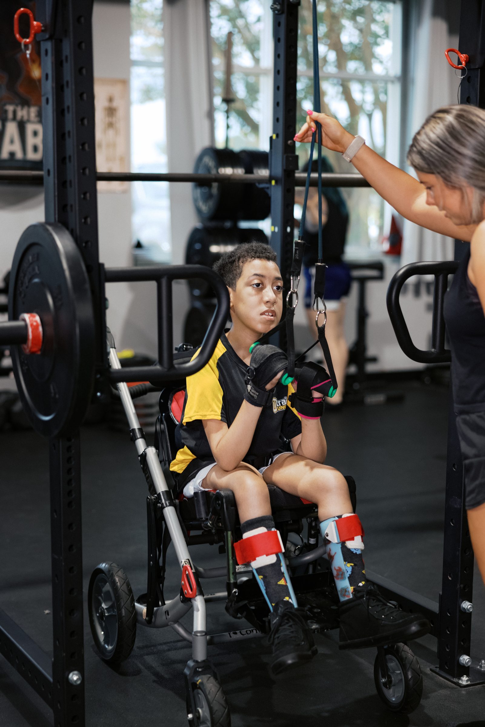 An athlete training in a standing frame at the squat rack, coach at her side